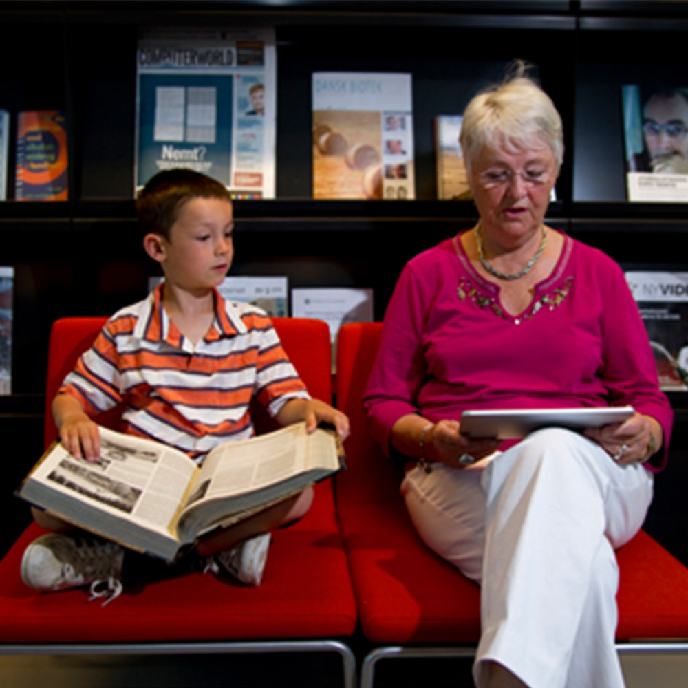 Child reading a book and an adult reading a tablet